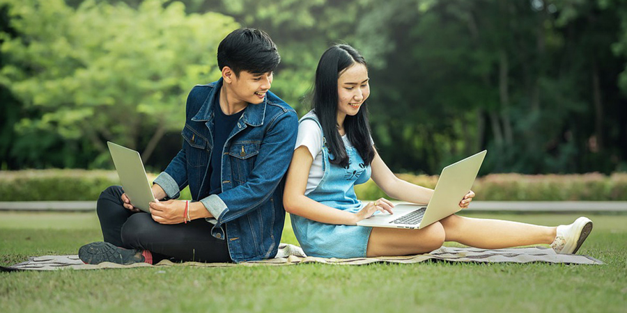 young man and woman using laptops in park
