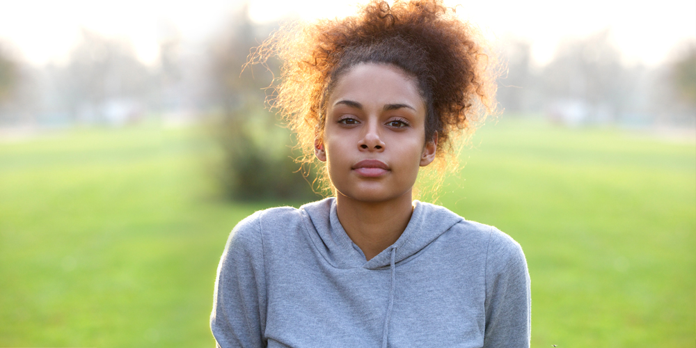 Beautiful lady in a gray hood sweater with expressionless face and direct stare on a grassy field