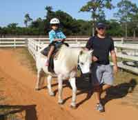 Child riding a pony while parent leads the pony